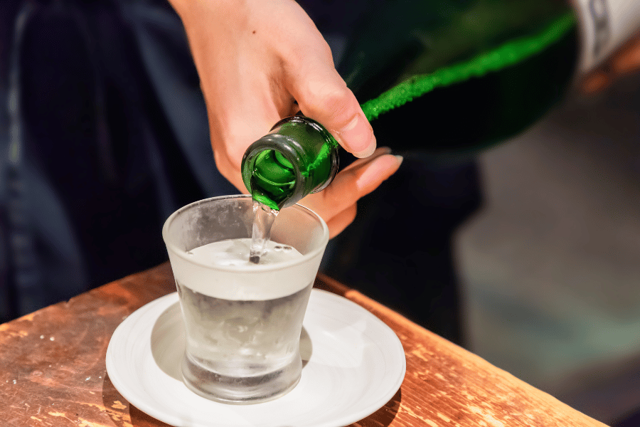 pouring sake into glass from green bottle