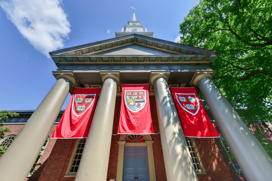 Harvard-University.png Harvard University buildings with Harvard flags on a sunny day